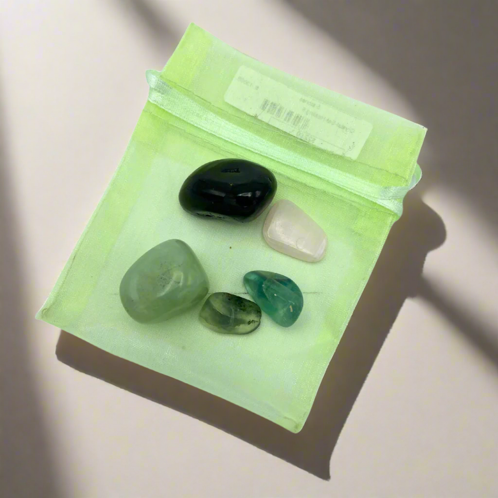 A selection of polished healing crystals in a small green bag The crystals include Prehnite, Fluorite, Shungite, Jadeite, and Mangano Calcite.