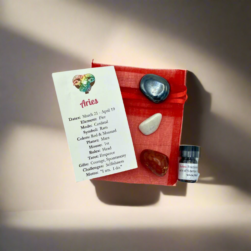 A red crystal pack labeled 'Aries Zodiac Crystal Pack' with three polished stones - Fire Agate, Hematite, and Howlite - along with small bottles of Siberian Fir and Lemon Essential Oils.