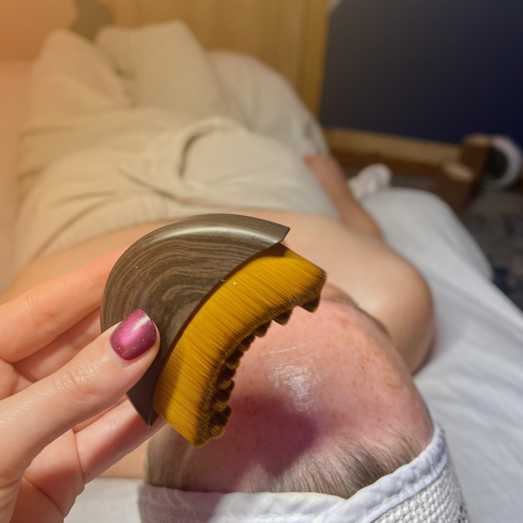 Person lying on a bed with a wooden and yellow lymphatic brush theld above them.