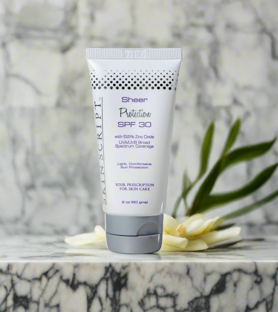Tube of SKINSCRIPTS Sheer Protection SPF 30 sunscreen with a marble background and a white flower.