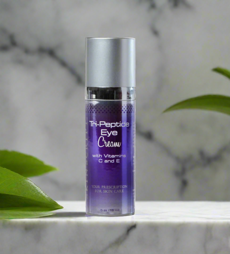 A bottle of SKINSCRIPTS Tri-Peptide Eye Cream with Vitamin C and E, placed on a marble surface with leaves in the background.