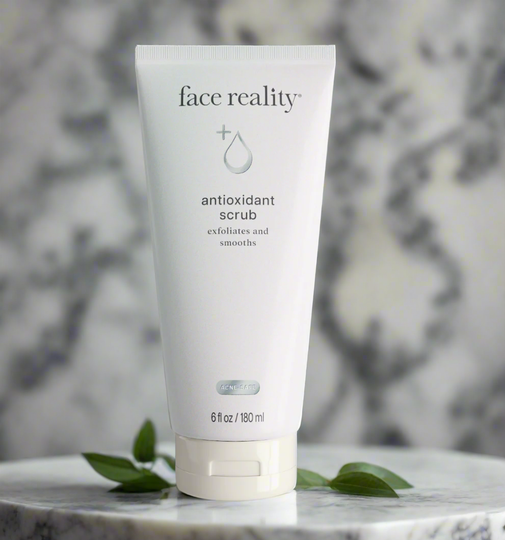 A tube of Face Reality Antioxidant Scrub with a white label on a marble background, accompanied by green leaves.