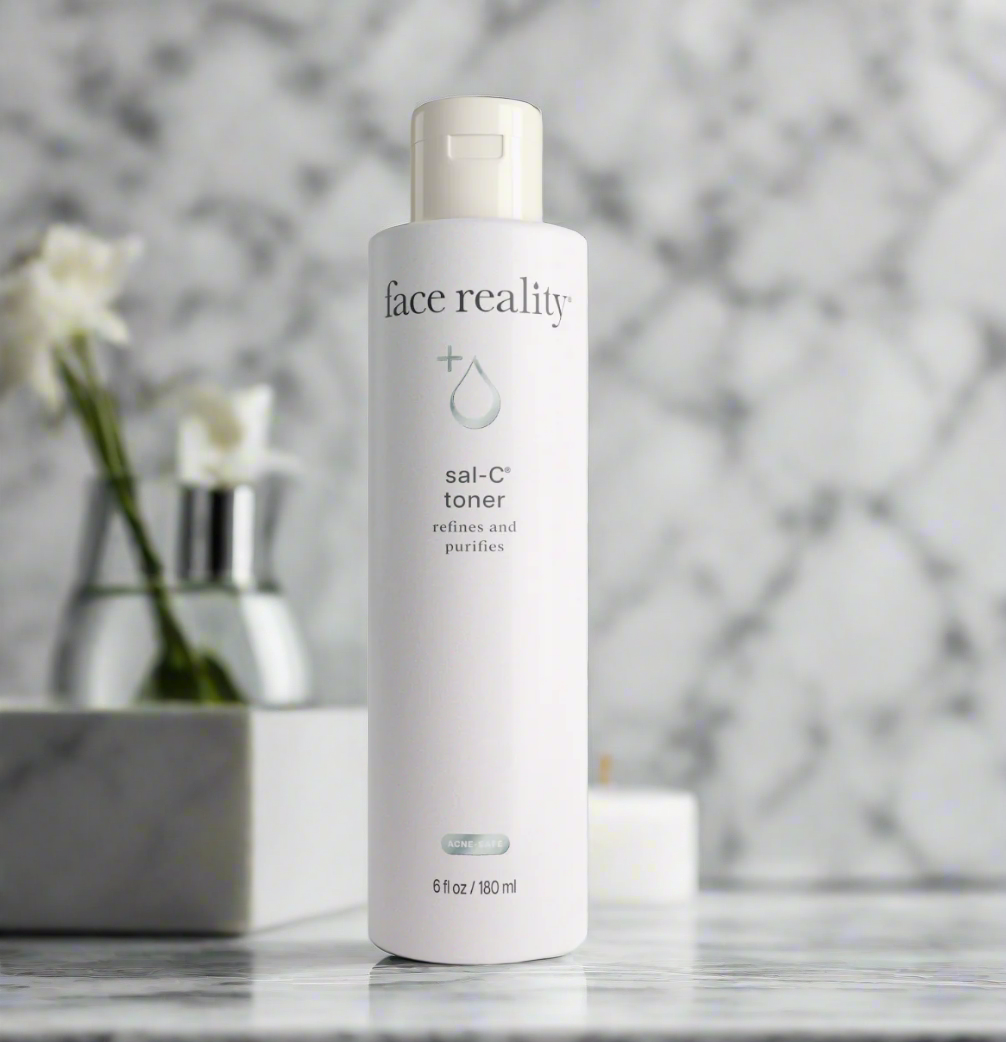 A bottle of Face Reality Sal-C Toner placed on a marble surface with a floral arrangement in the background.