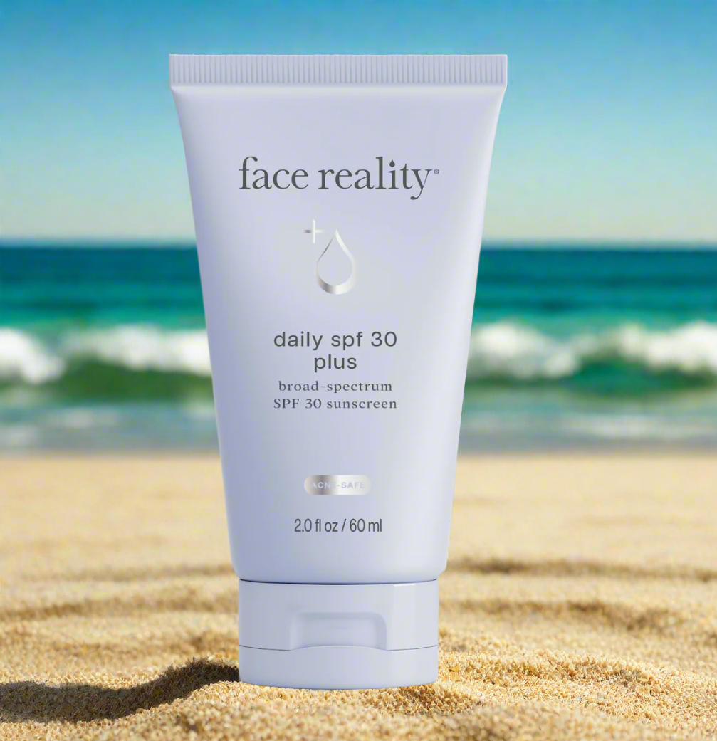 Tube of Face Reality Daily SPF 30 Plus sunscreen positioned on a sandy beach with ocean and sky in the background.