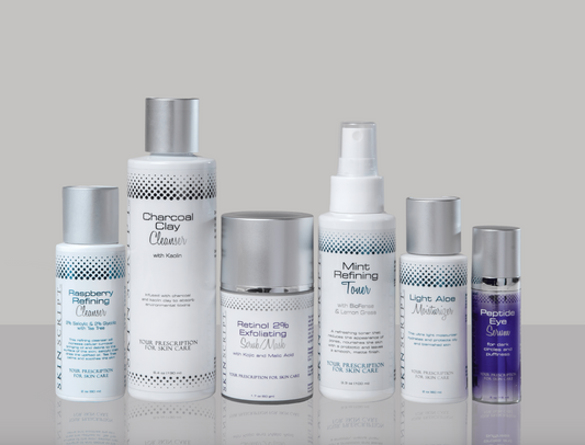 A collection of skincare products including cleansers, exfoliating scrub, toner, eye serum, and moisturizer, arranged in a row with their respective labels.