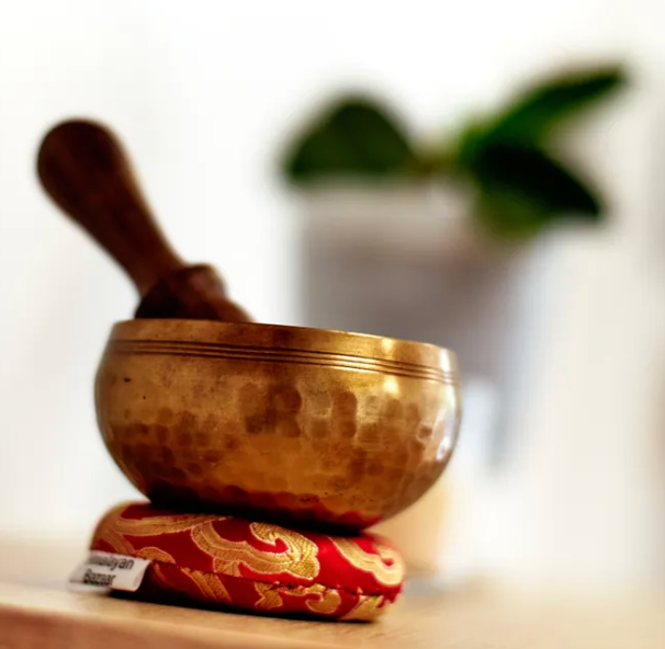 Tibetan singing bowl with a wooden striker on a red cushion, blurred background